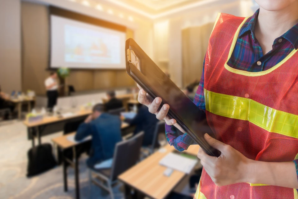 Salle de formation professionnelle avec personne en gilet de sécurité haute visibilité rouge et jaune consultant une tablette numérique