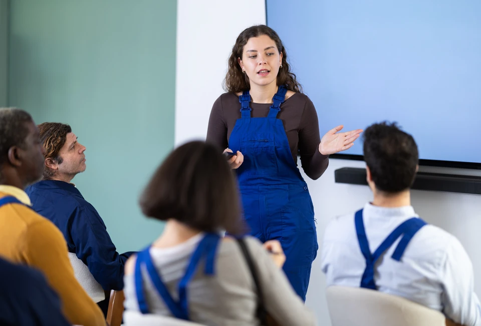 Formateur ou consultant professionnel en tenue professionnelle (costume/chemise) en train de dispenser une formation ou présenter un contenu pédagogique devant un groupe d'apprenants assis en salle de formation, utilisant un support visuel ou tableau blanc. L'ambiance doit être sérieuse, professionnelle et clairement pédagogique, illustrant l'expertise et l'autorité de l'intervenant dans un contexte de formation en entreprise.