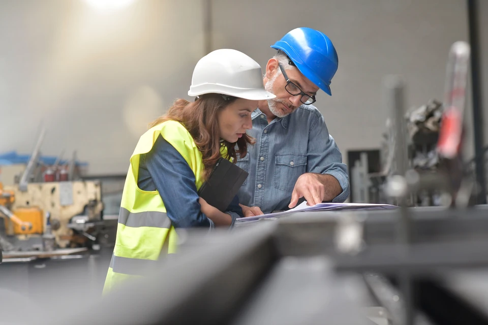 Deux professionnels en équipements de sécurité examinent des plans techniques dans un environnement industriel