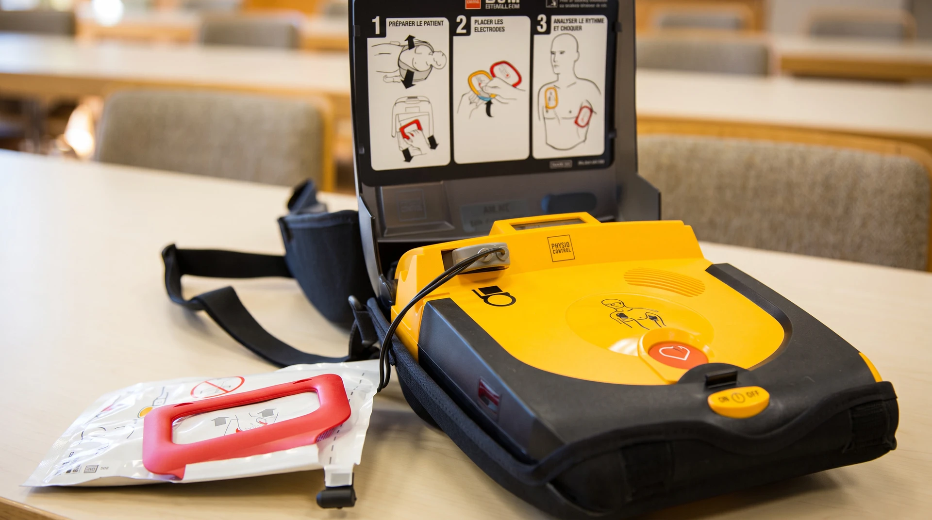 Scène intérieure de formation aux premiers secours avec défibrillateur automatisé externe (DAE) jaune et noir posé sur une table