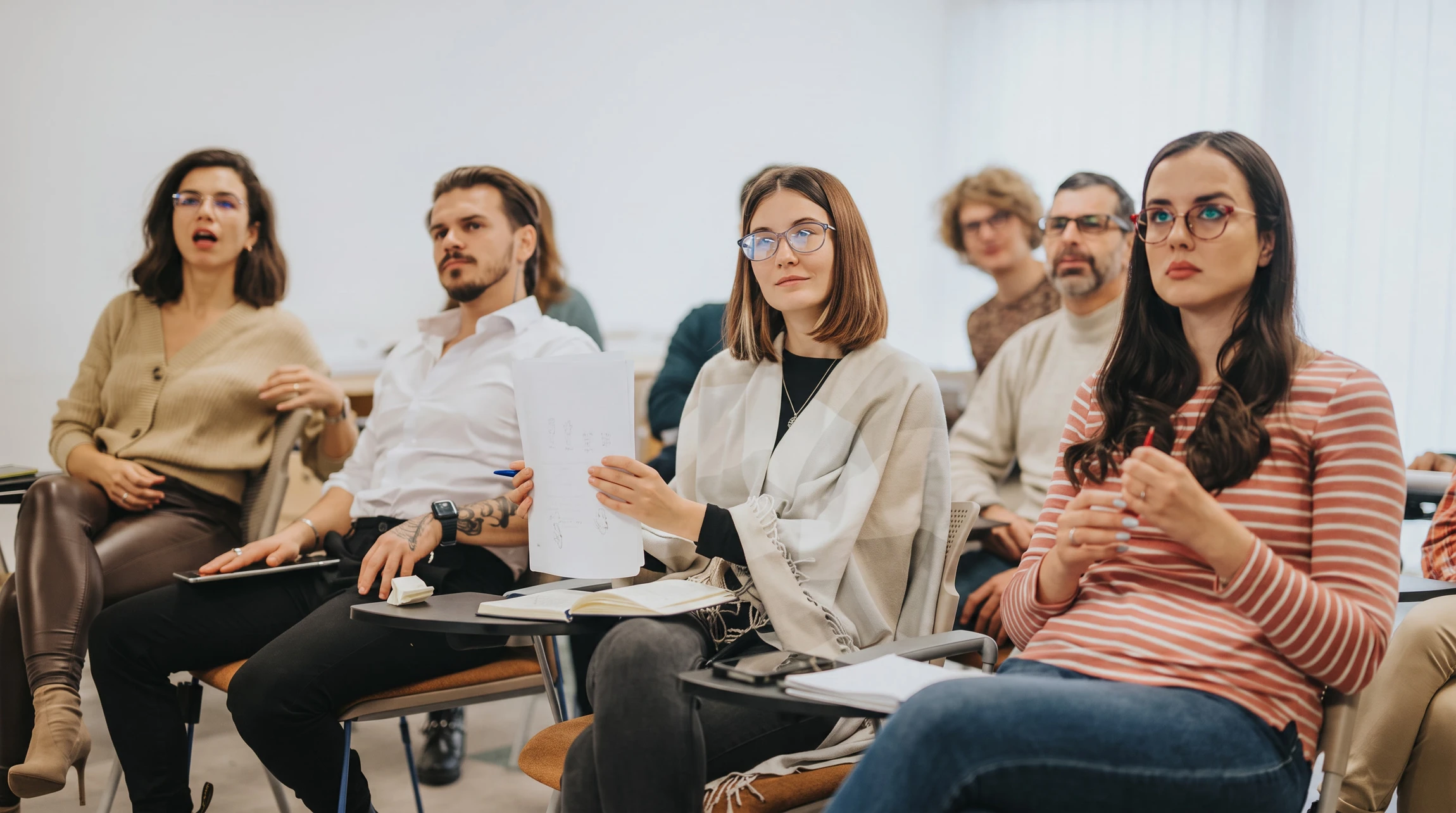 Salle de formation moderne avec groupe de professionnels assis en rangées, suivant attentivement une présentation