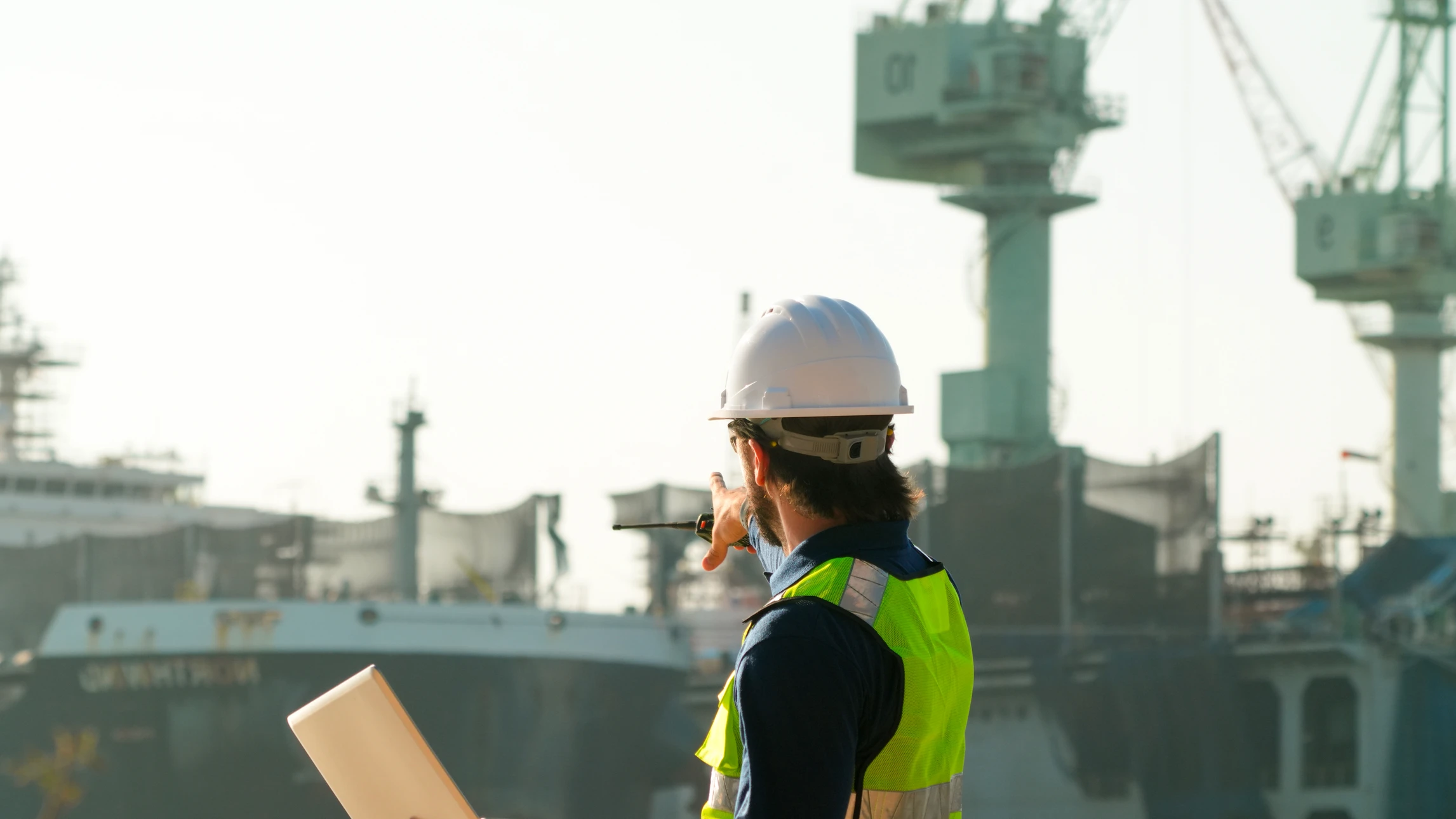 Scène extérieure sur site industriel avec technicien en équipement de protection individuelle complet manipulant des big-bags de déchets radioactifs